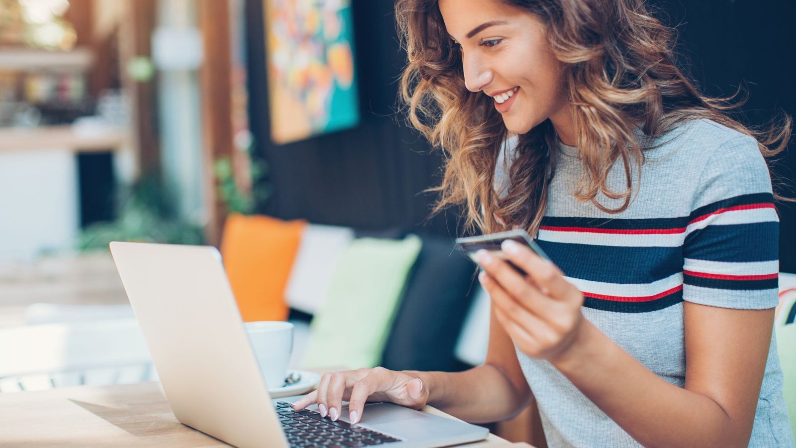 Jeune femme souriante avec une carte bleue en main en train de réaliser un achat sur internet