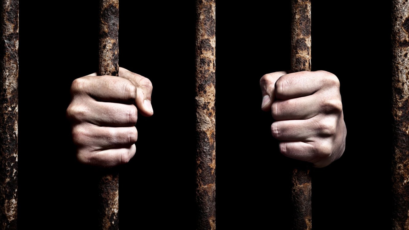 Photo de mains accrochées aux barreaux d'une prison.